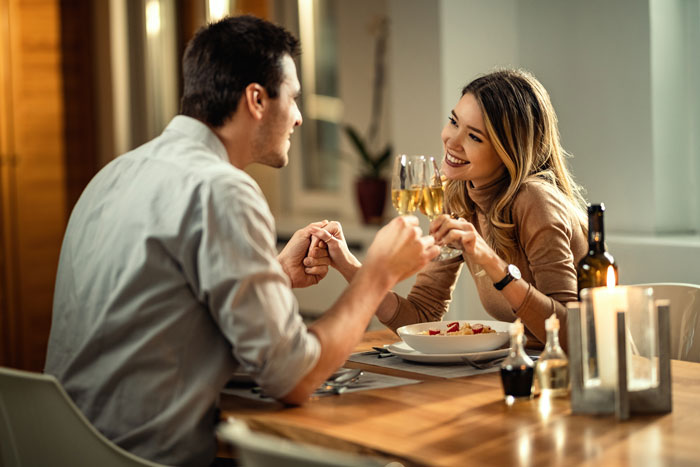 Couple holding hands over dinner table on first date, woman expressing no spark while man reacts demanding meal payment.
