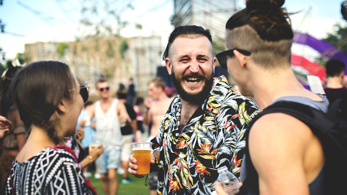Man laughing with friends at outdoor Glastonbury festival holding a beer, capturing the festival atmosphere and crowd.