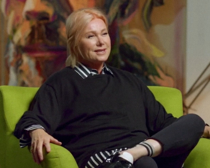 Woman with blonde hair sitting casually in a green chair, discussing Hugh Jackman and Sutton Foster’s 17-year history. Woman with blonde hair sitting casually in a green chair, discussing Hugh Jackman and Sutton Foster’s 17-year history.