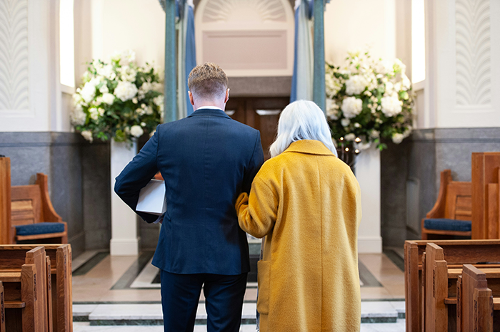 Man in suit and woman in yellow coat walking down aisle in funeral home, reflecting concern about lawsuit and legal advice.