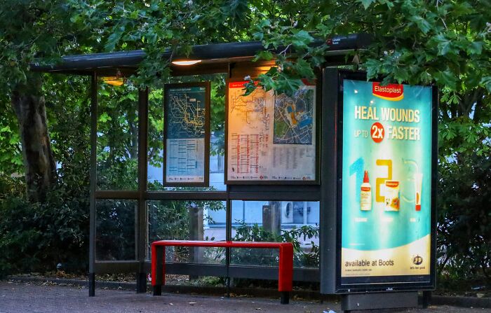 Bus stop at night with illuminated ads, surrounded by trees, illustrating moments of people ruining their life with one wrong deed.
