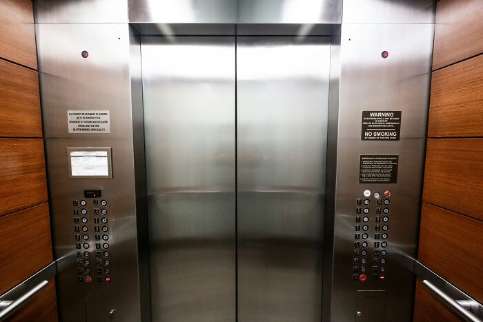 Elevator interior with stainless steel doors and wood paneling, highlighting unusual public behavior spaces.