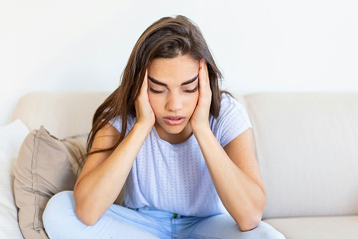 Woman stressed and upset, sitting on couch with hands on her head, refusing to risk her health for family wedding photo. Woman stressed and upset, sitting on couch with hands on her head, refusing to risk her health for family wedding photo.