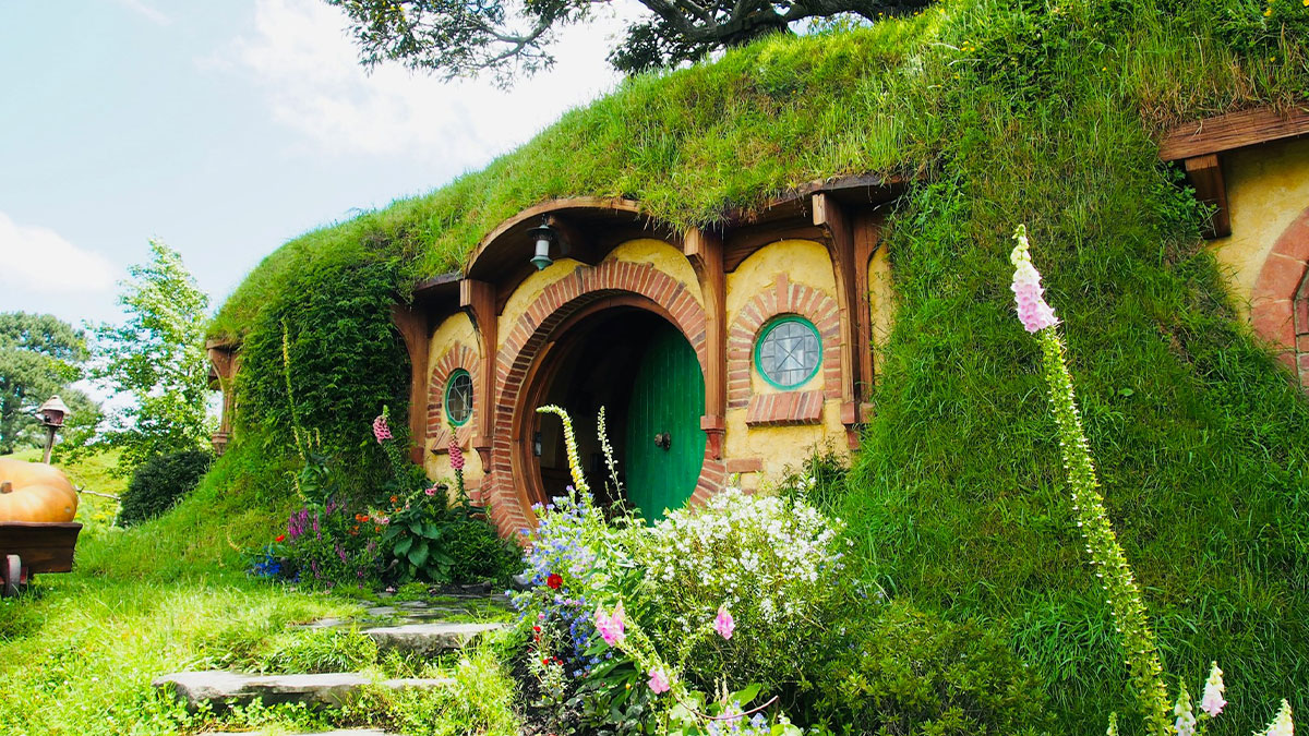 Hobbit-style house with round door and grassy roof surrounded by flowers in a travel destination tourists suggest avoiding.