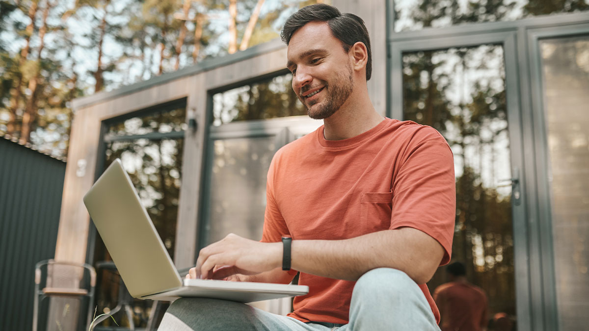 Man smiling and using laptop outdoors, illustrating a job referral after ghosting friend post-divorce scenario
