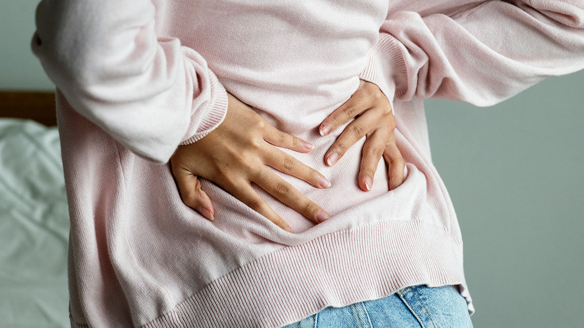 Person in pink sweater holding lower back in pain, illustrating symptoms related to medical conditions.