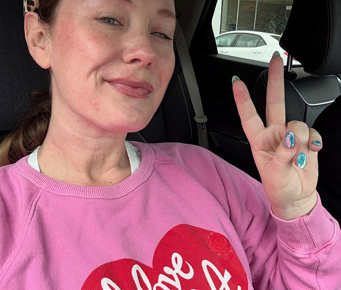 Woman in a pink sweatshirt making a peace sign inside a car, related to Tom Hanks breaking silence after daughter’s claims. Woman in a pink sweatshirt making a peace sign inside a car, related to Tom Hanks breaking silence after daughter’s claims.