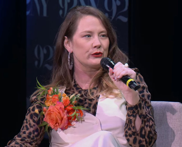 Woman holding microphone and orange flowers, speaking during a discussion about Tom Hanks and childhood struggles revealed by daughter. Woman holding microphone and orange flowers, speaking during a discussion about Tom Hanks and childhood struggles revealed by daughter.