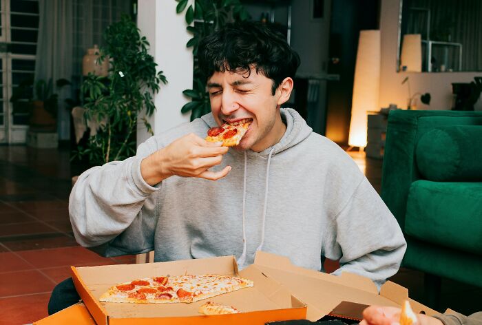 Young man enjoying pizza at home, capturing a priceless reward moment after spending just a dollar.