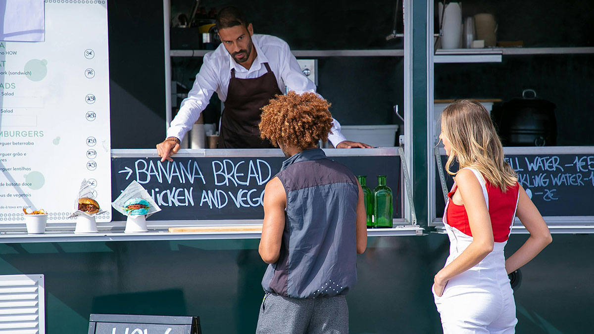A lady tries to jump the line at a fast food truck, accidentally reaching for another man's takeout order.