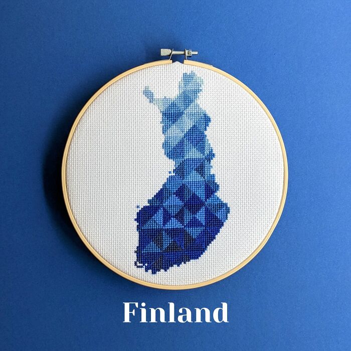 Cross-stitched map of Finland in shades of blue displayed in an embroidery hoop on a blue background.
