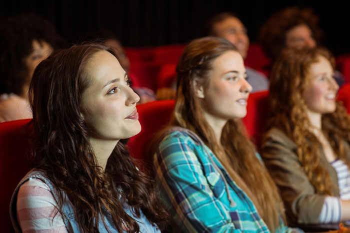Young women seated in a theater, watching a drama about an ex and narcissist causing conflict in relationships. Young women seated in a theater, watching a drama about an ex and narcissist causing conflict in relationships.