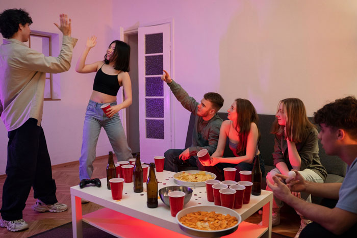 Group of young people at a party, a man interacting with a girl, others sitting and watching with drinks on the table. Group of young people at a party, a man interacting with a girl, others sitting and watching with drinks on the table.