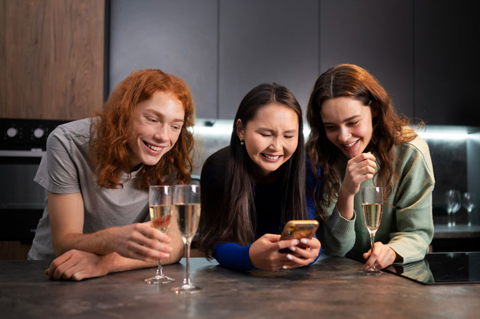 Three friends laughing together in a kitchen, representing a squad secretly disliking someone's boyfriend. Three friends laughing together in a kitchen, representing a squad secretly disliking someone's boyfriend.
