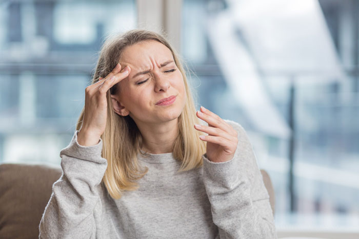 Woman in a gray sweater showing discomfort and headache, illustrating risks of prolonged fasting in a modern indoor setting. Woman in a gray sweater showing discomfort and headache, illustrating risks of prolonged fasting in a modern indoor setting.