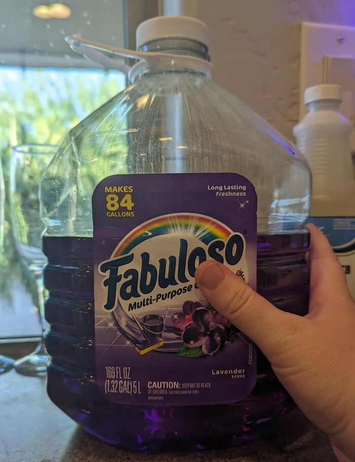 Hand holding a large purple Fabuloso bottle, illustrating coworker diabolical things in an office or home setting.
