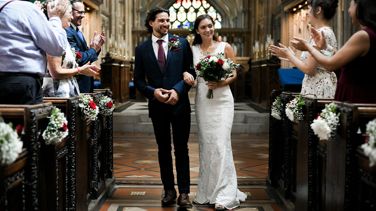 Bride and groom walking down aisle in elegant wedding ceremony with guests clapping inside decorated church venue