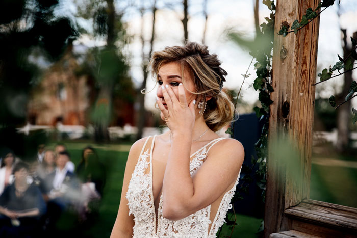 Bride in lace wedding dress wiping tears during outdoor ceremony, highlighting shock of mother of ring bearer left off guest list. Bride in lace wedding dress wiping tears during outdoor ceremony, highlighting shock of mother of ring bearer left off guest list.