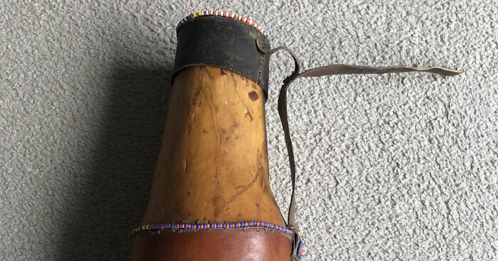 Weirdest item owned, a vintage wooden and leather animal horn with a beaded rim and attached strap on carpet background.