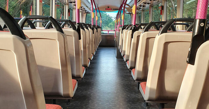 Interior view of empty public transport bus showing rows of beige seats and windows with natural light.
