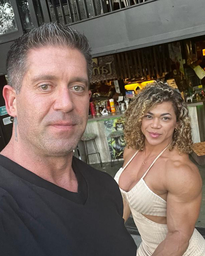 Man and muscular woman posing for a selfie at a cafe, highlighting bodybuilder dubbed she hulk in public setting. Man and muscular woman posing for a selfie at a cafe, highlighting bodybuilder dubbed she hulk in public setting.