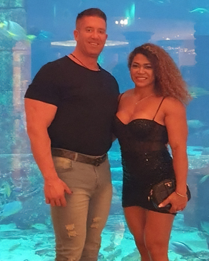 Bodybuilder dubbed She Hulk posing with a man, both smiling in front of an aquarium background.