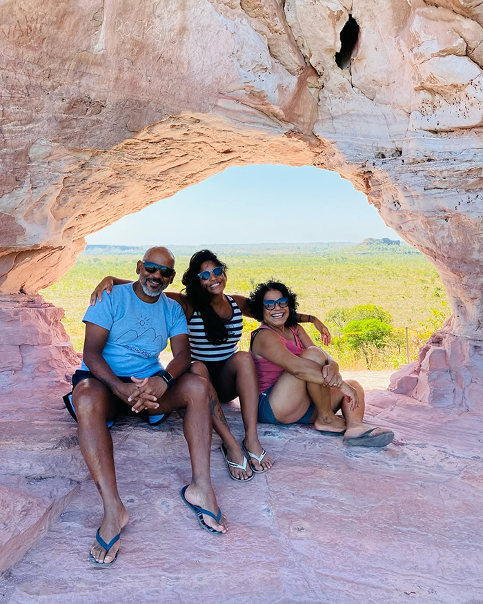 Three tourists sitting inside a natural rock arch with a scenic view, unrelated to being trapped inside an active volcano. Three tourists sitting inside a natural rock arch with a scenic view, unrelated to being trapped inside an active volcano.