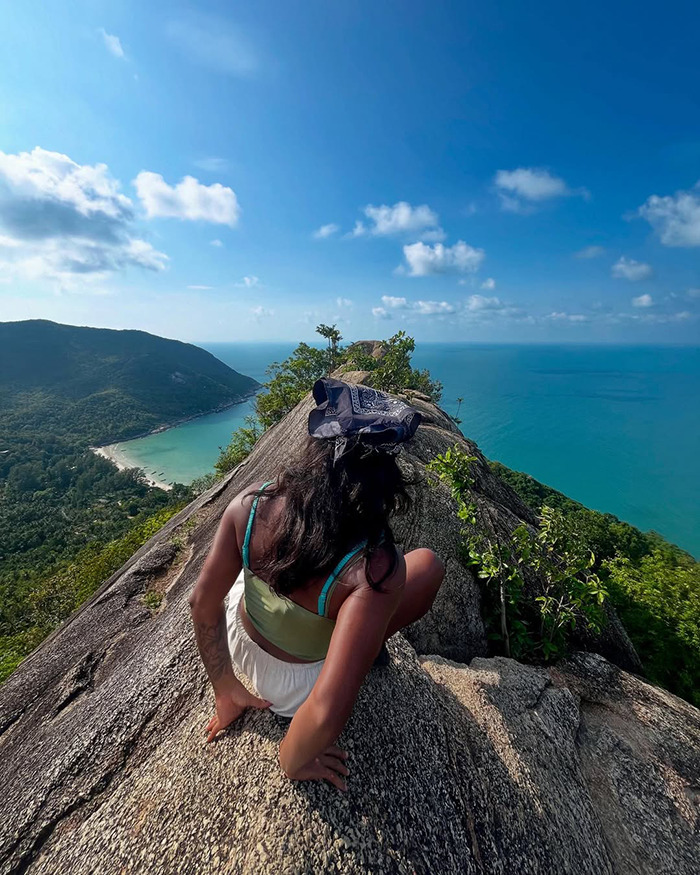 Woman sitting on rocky cliff overlooking ocean and green hills, symbolizing tourist trapped inside active volcano. Woman sitting on rocky cliff overlooking ocean and green hills, symbolizing tourist trapped inside active volcano.