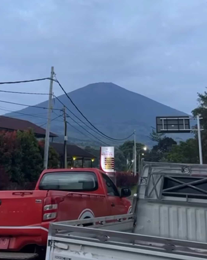 Red pickup trucks parked on street with active volcano visible in the background on a cloudy day. Red pickup trucks parked on street with active volcano visible in the background on a cloudy day.