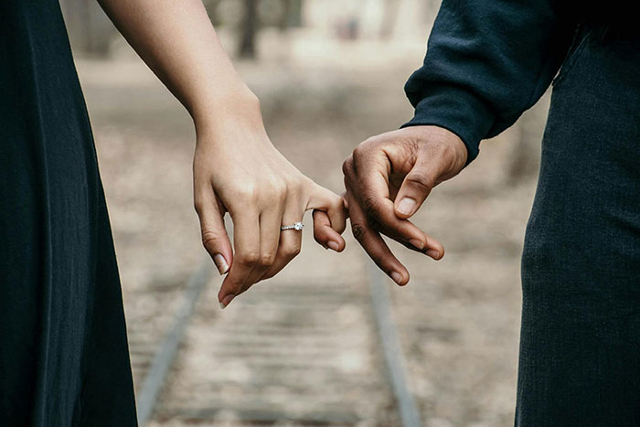 Close-up of a couple holding pinky fingers with a focus on the bride's engagement ring symbolizing groom-to-be cold feet jokes. Close-up of a couple holding pinky fingers with a focus on the bride's engagement ring symbolizing groom-to-be cold feet jokes.