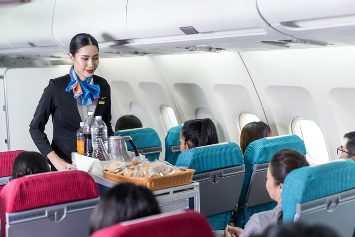 Flight attendant serving passengers in airplane cabin while managing sensitive safety questions from a passenger. Flight attendant serving passengers in airplane cabin while managing sensitive safety questions from a passenger.