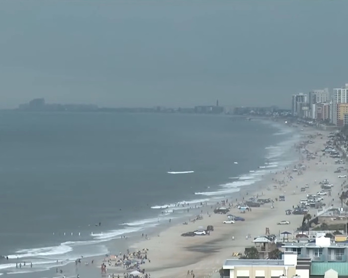 A crowded beach scene with people near the water, highlighting a newlywed’s honeymoon tragedy near ankle-deep water. A crowded beach scene with people near the water, highlighting a newlywed’s honeymoon tragedy near ankle-deep water.