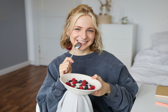 Young woman eating a bowl of fiber-rich berries, promoting the body’s ability to get rid of cancer-causing forever chemicals Young woman eating a bowl of fiber-rich berries, promoting the body’s ability to get rid of cancer-causing forever chemicals