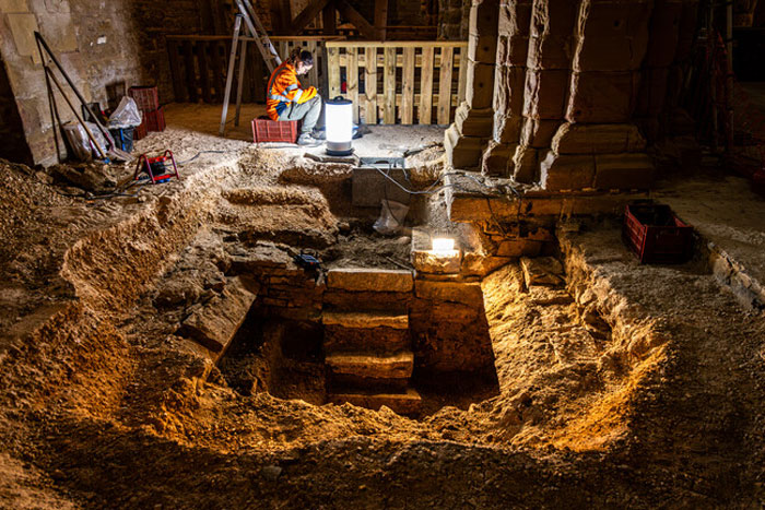 Archaeologist in safety vest examining a 400-year-old burial vault accidentally uncovered during church restoration. Archaeologist in safety vest examining a 400-year-old burial vault accidentally uncovered during church restoration.
