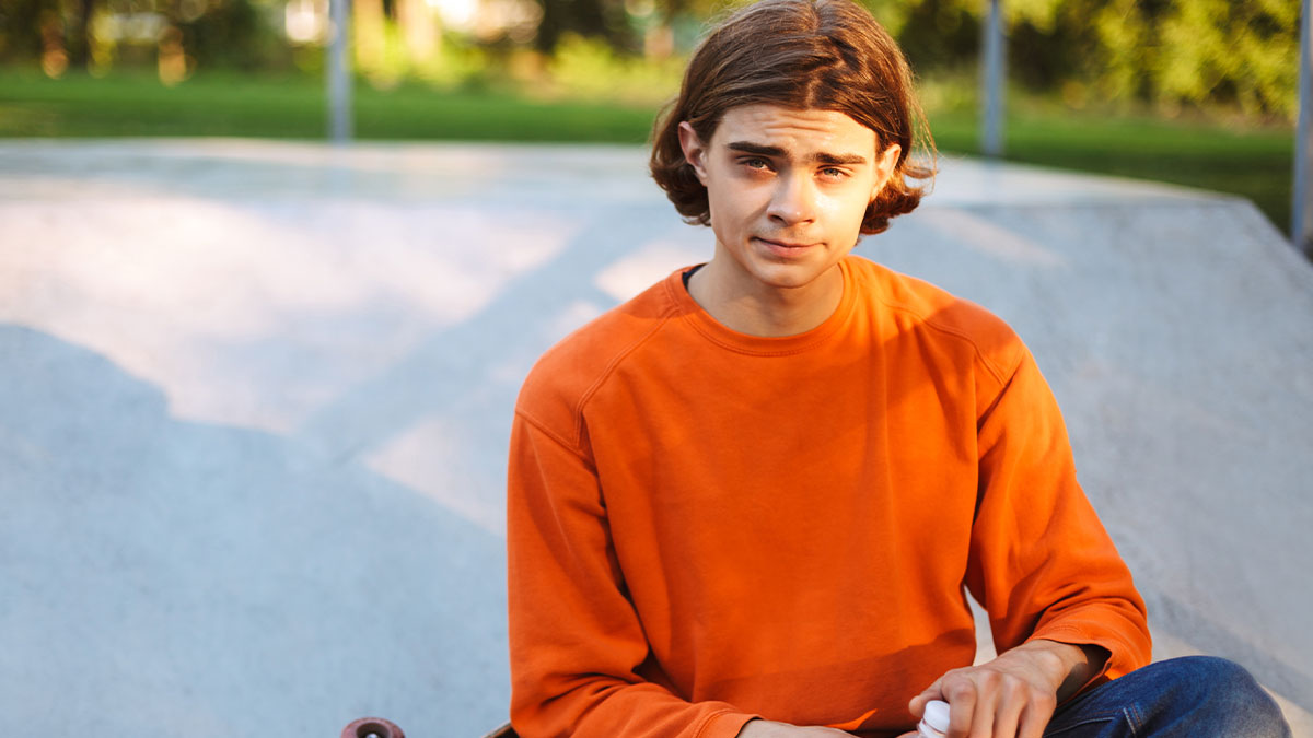 Teen in an orange sweatshirt looking confused outdoors after foster parents suggest his name isnu2019t respectable enough to keep.