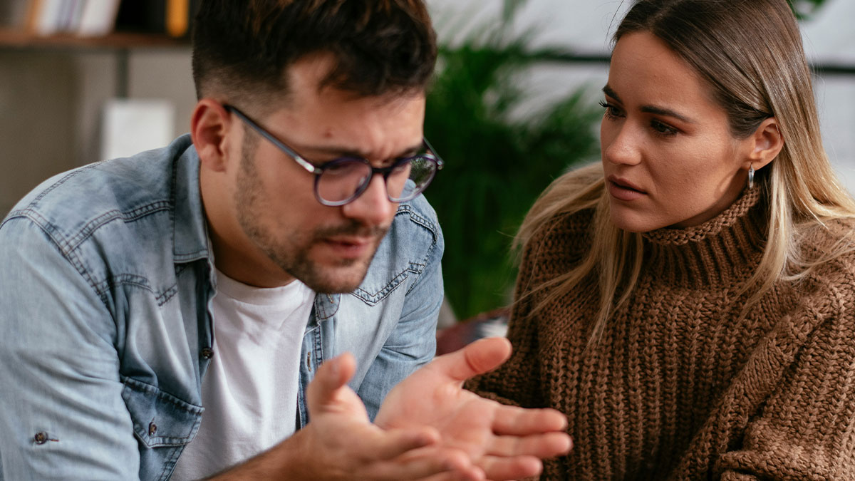 Man explaining something with upset expression while woman listens closely in a friend claims cat name newborn discussion.