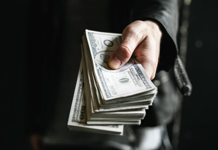 Hand holding a stack of hundred dollar bills symbolizing inheritance and financial dispute between best friends.