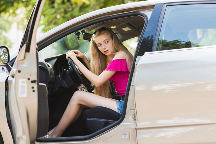 Teen girl with long blonde hair sitting in the driver's seat of a car, ready to drive to a friend stepdaughter pool party.