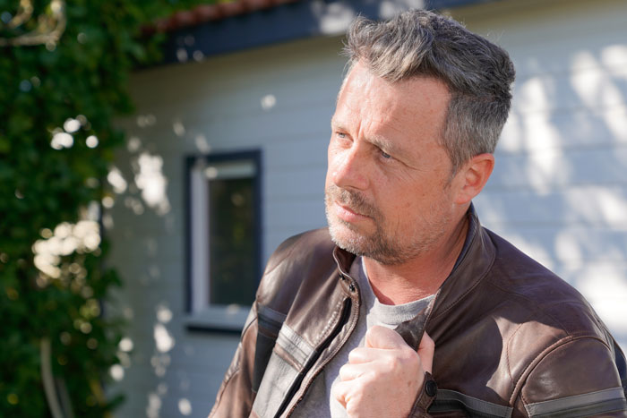 Middle-aged man in a leather jacket outdoors reflecting thoughtfully at a friend stepdaughter pool party setting.