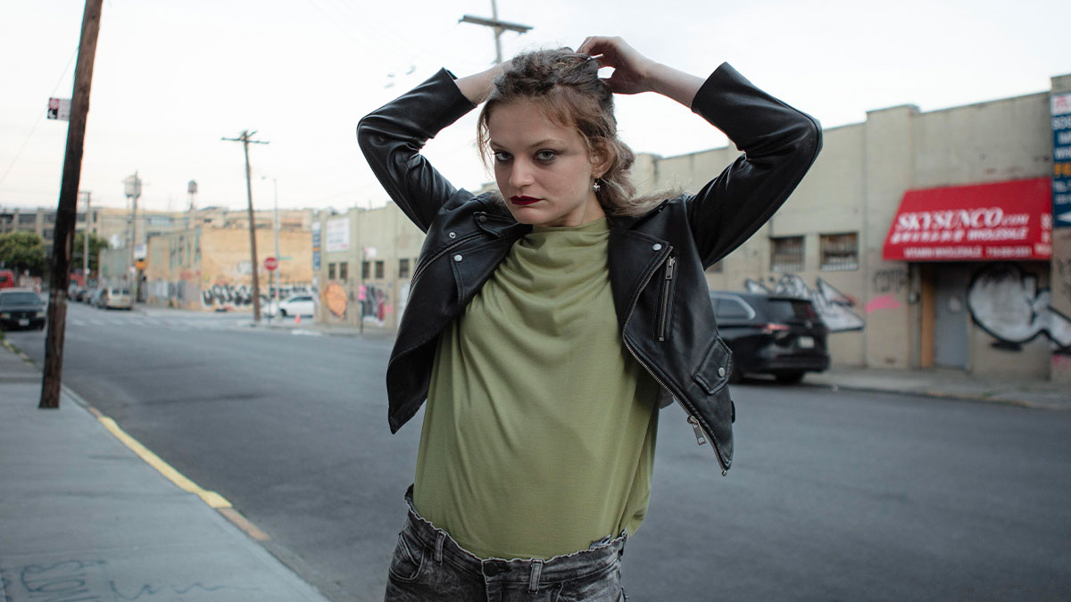 Teen with frustrated expression outdoors, wearing a leather jacket and green shirt, showing a hissy fit mood.