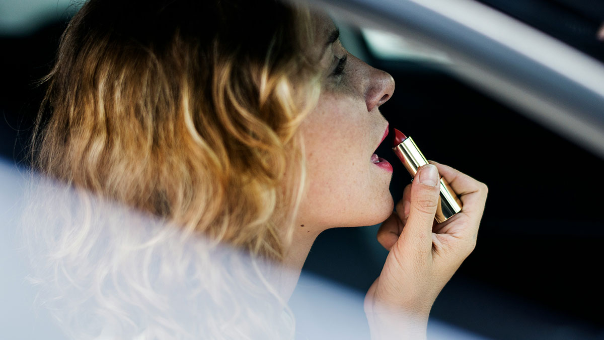 Woman applying lipstick in a car, capturing a relatable moment from funny mom posts about daily life and sanity breaks.