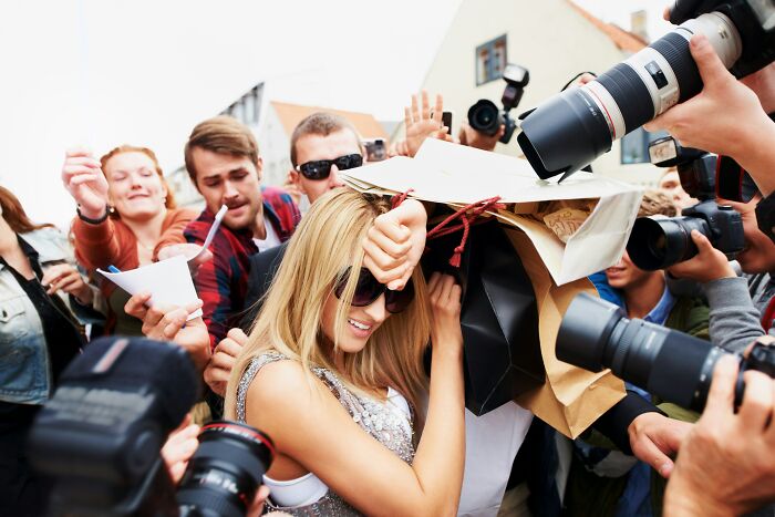 A woman shielding herself from a crowd of photographers and fans highlighting professions attracting awful people.