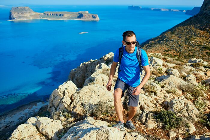 Man hiking rocky coast with blue sea and islands in background, illustrating European netizens correcting common country facts.