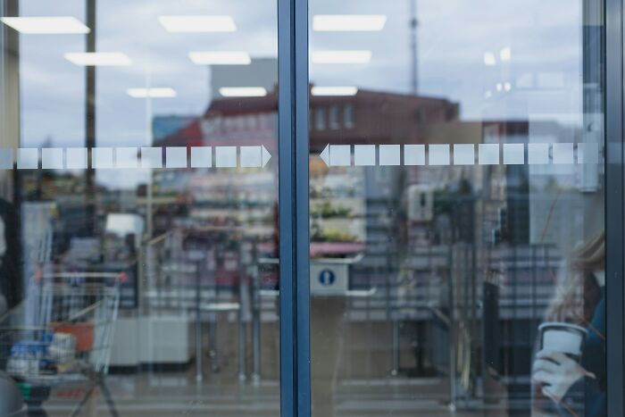 Reflection on glass doors of a public place showing a shopping cart and blurred urban surroundings in the background.