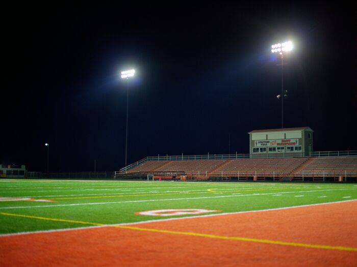 Empty football field at night under bright stadium lights, symbolizing a priceless reward after a small investment.