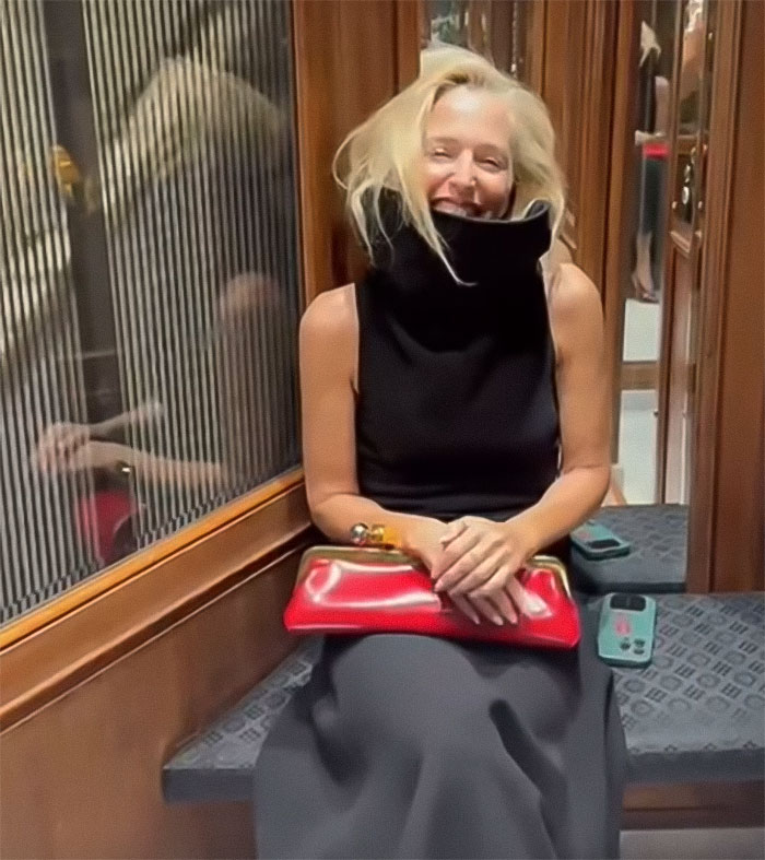 Woman in a black sleeveless outfit holding a red clutch, smiling while sitting in an elevator near a wooden wall. Woman in a black sleeveless outfit holding a red clutch, smiling while sitting in an elevator near a wooden wall.