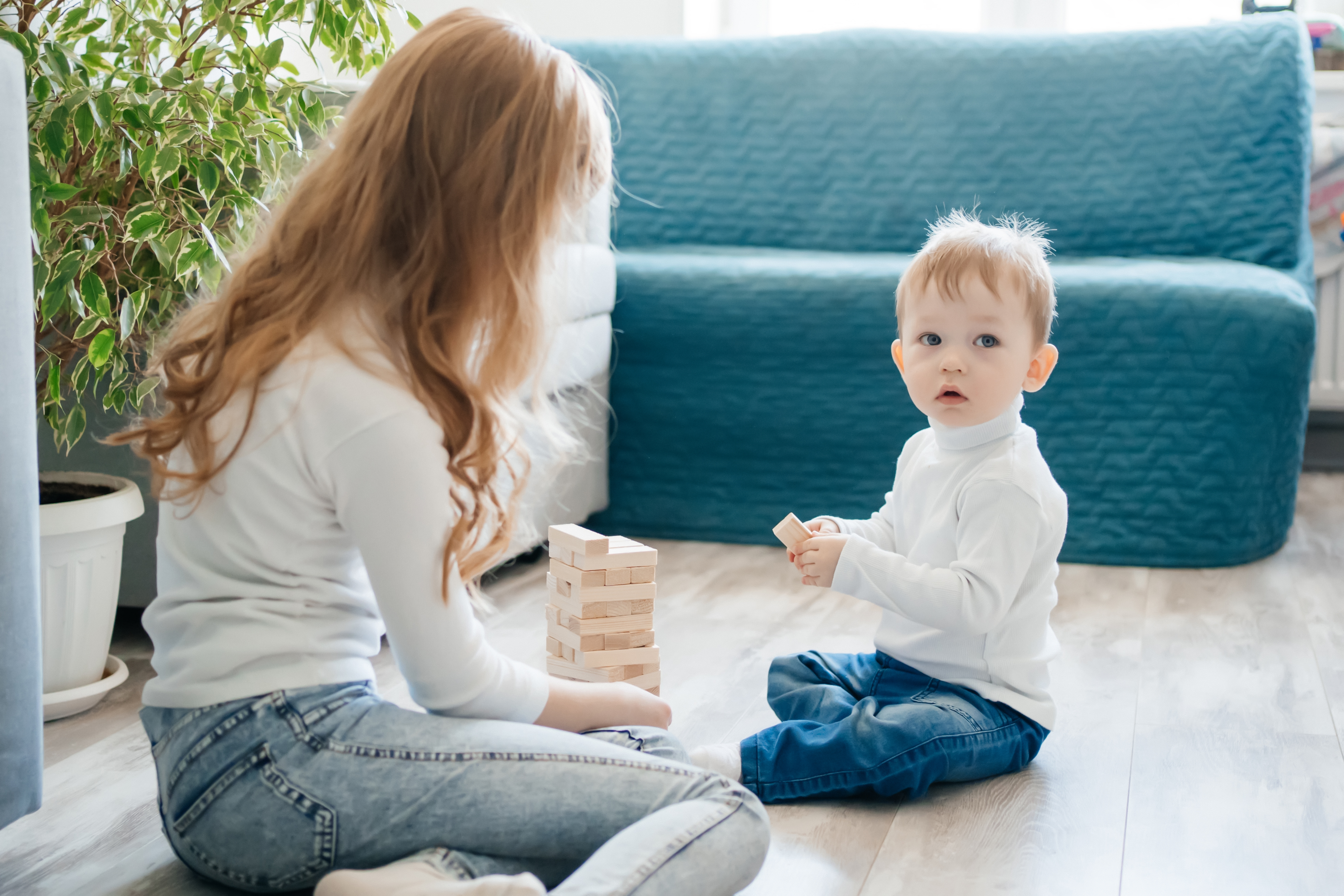 Young woman babysitting child at home playing with wooden blocks on floor during summer care time Young woman babysitting child at home playing with wooden blocks on floor during summer care time