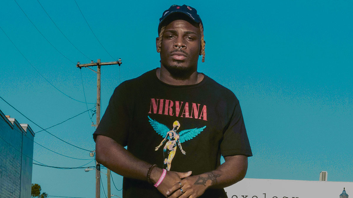 Young man wearing a Nirvana t-shirt and cap standing outdoors under a clear blue sky, reflecting on girlfriend behaviour change relationship.