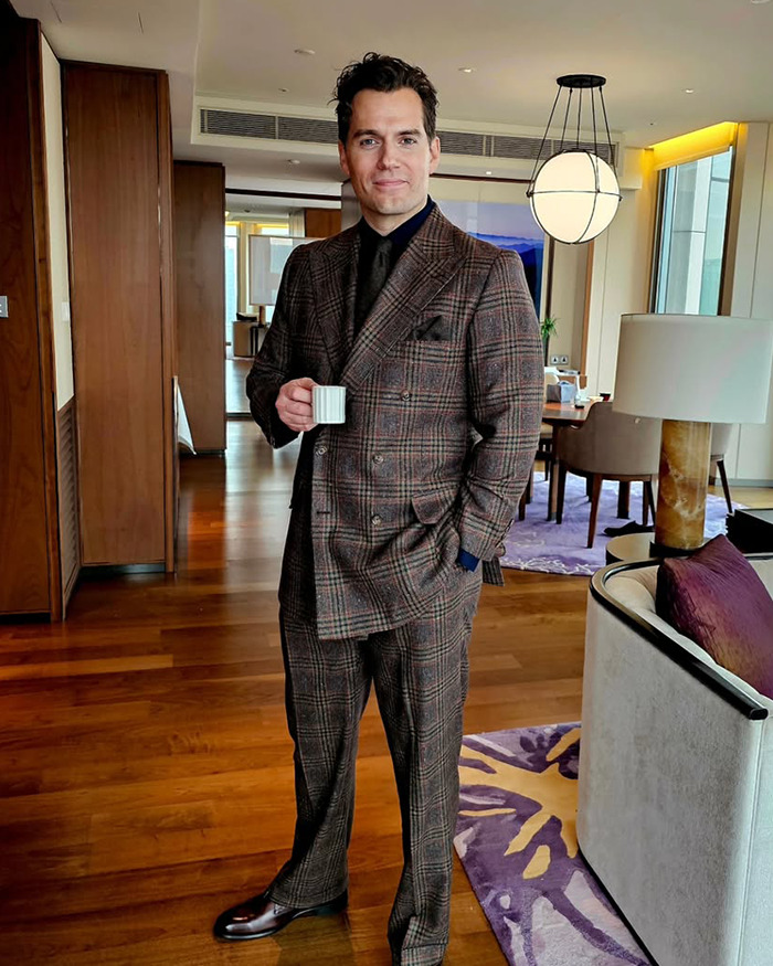 Henry Cavill in a brown plaid suit holding a cup indoors, showcasing his new Highlander hairstyle attracting fan attention. Henry Cavill in a brown plaid suit holding a cup indoors, showcasing his new Highlander hairstyle attracting fan attention.