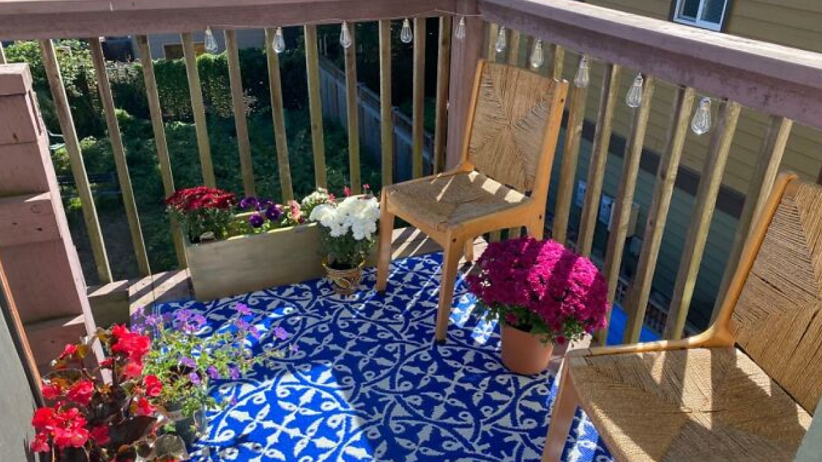 Small balcony with colorful flowers, wooden chairs, and a patterned blue rug for hiding home uglies.